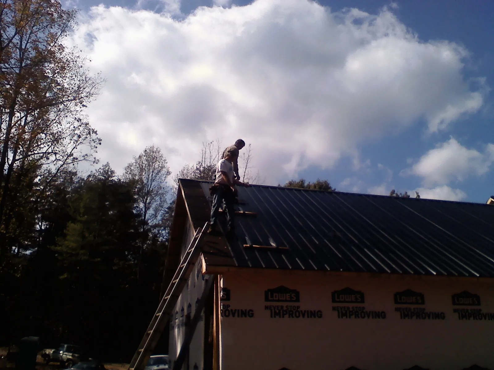 Roofer fastening dark metal panels high against a cloudy sky, from a Roof Inspection job in Bloomington