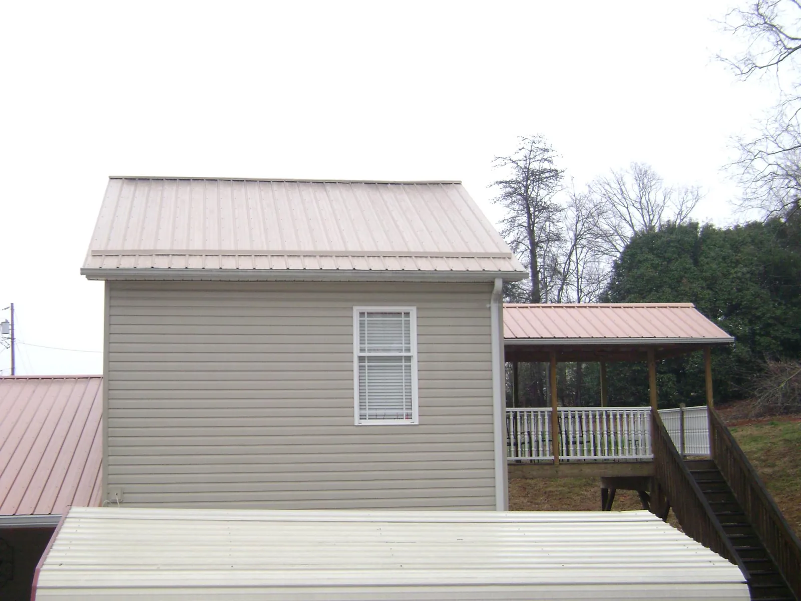 Tan metal roofs on a two story addition and attached porch, from a Roof Replacement job in Bloomington