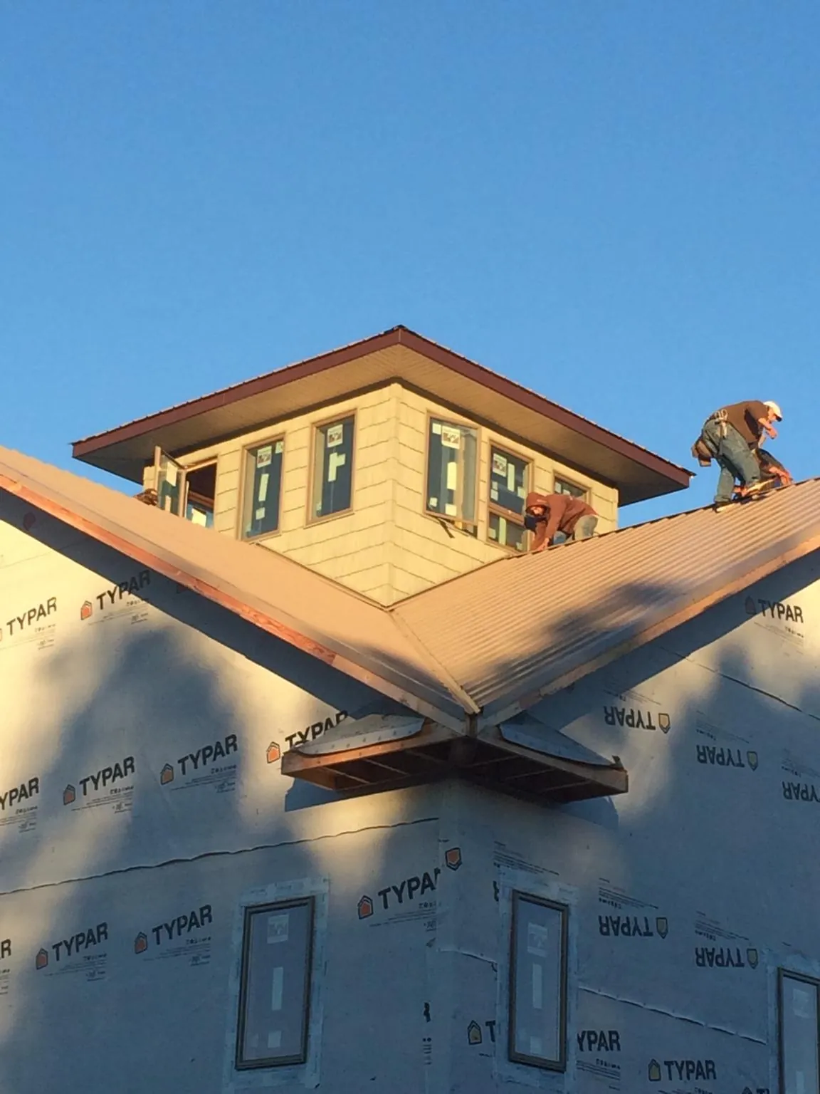 Roofers working around a rooftop cupola on a new metal roof at sunset — Roof Waterproofing in Bloomington by Roofing Brothers